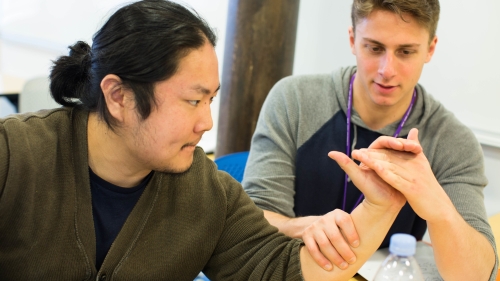 Two occupational therapy students do a wrist exercise together.